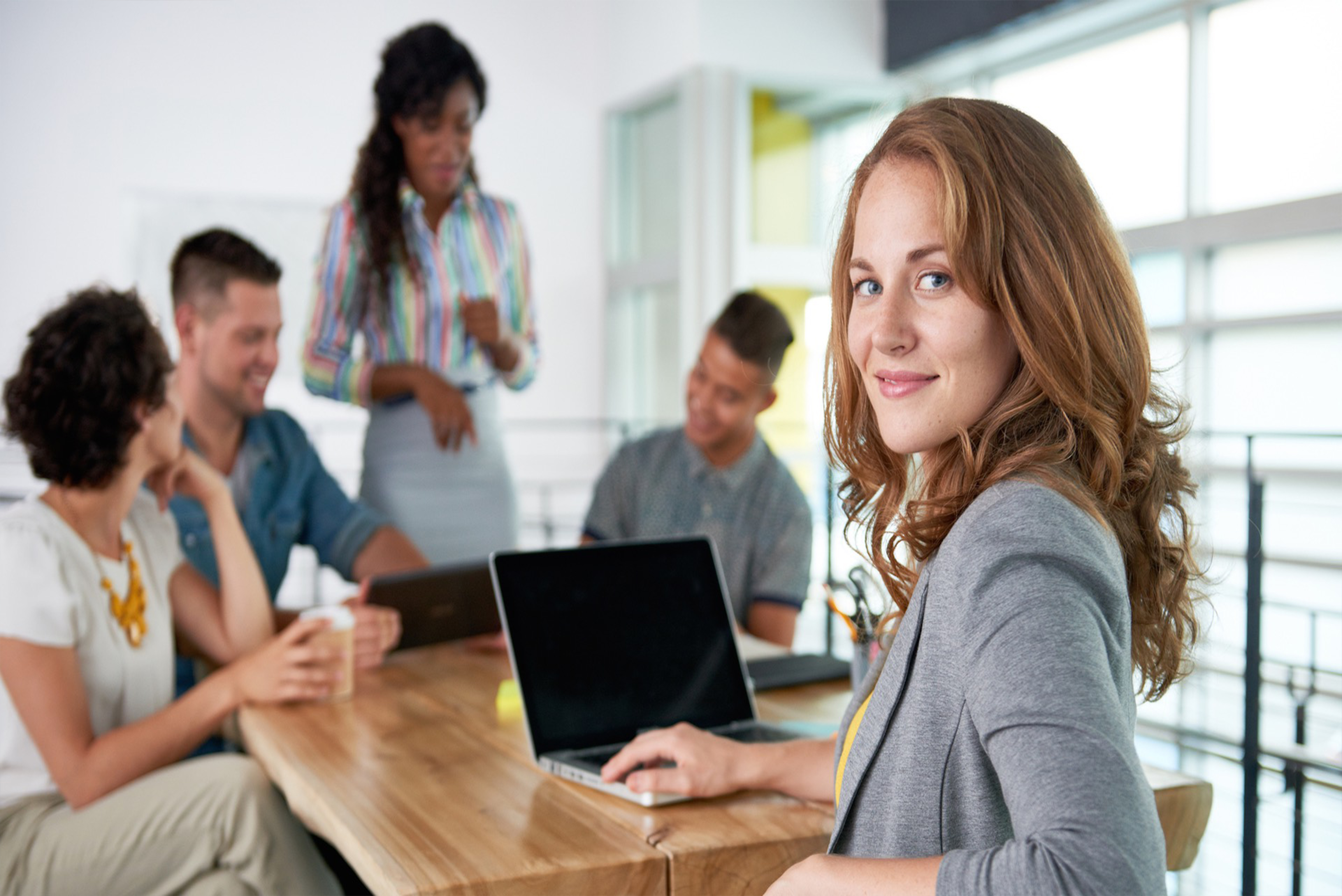 women sitting at wooden table with other people and computer