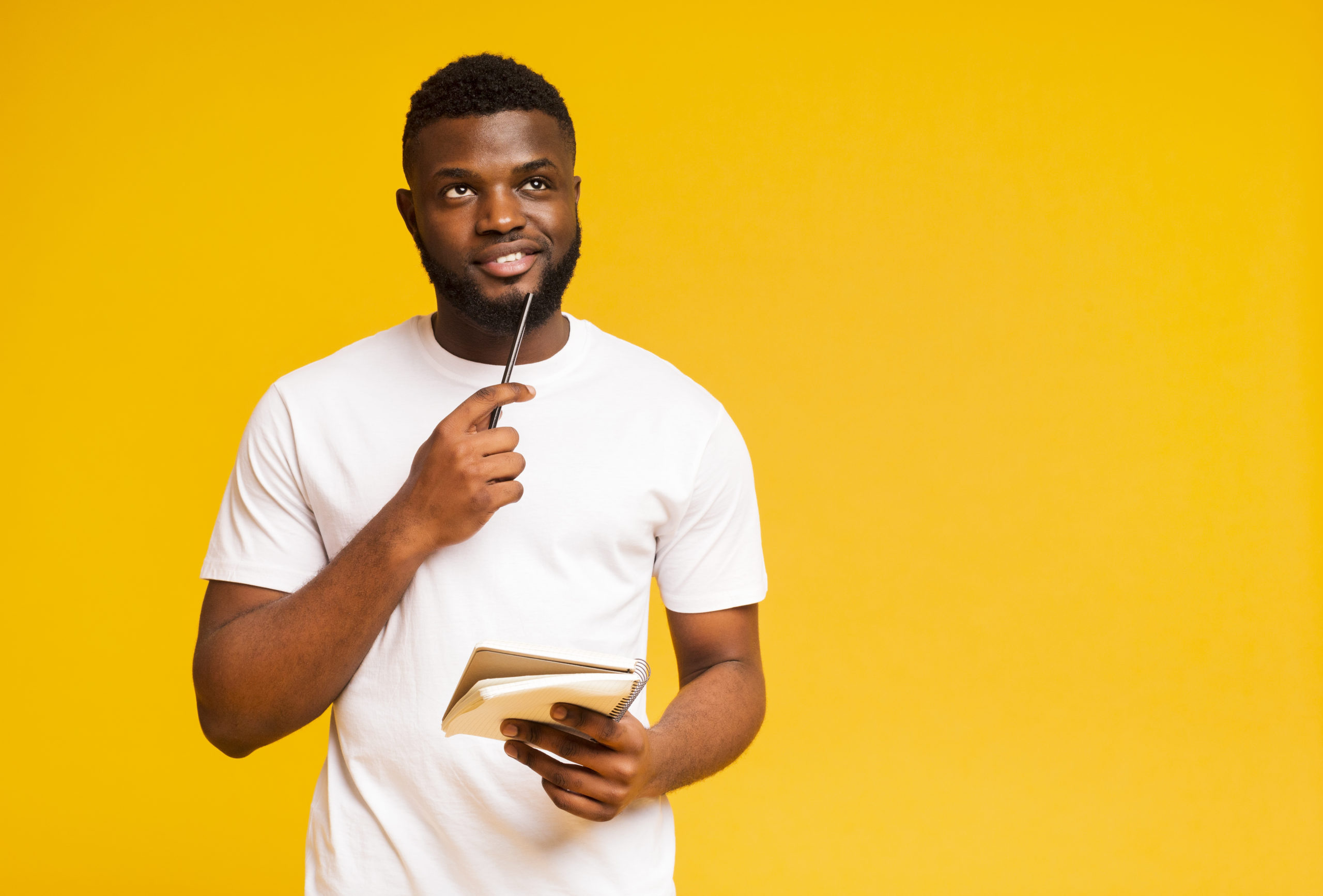 Pensive african guy taking notes, writing check list in notebook